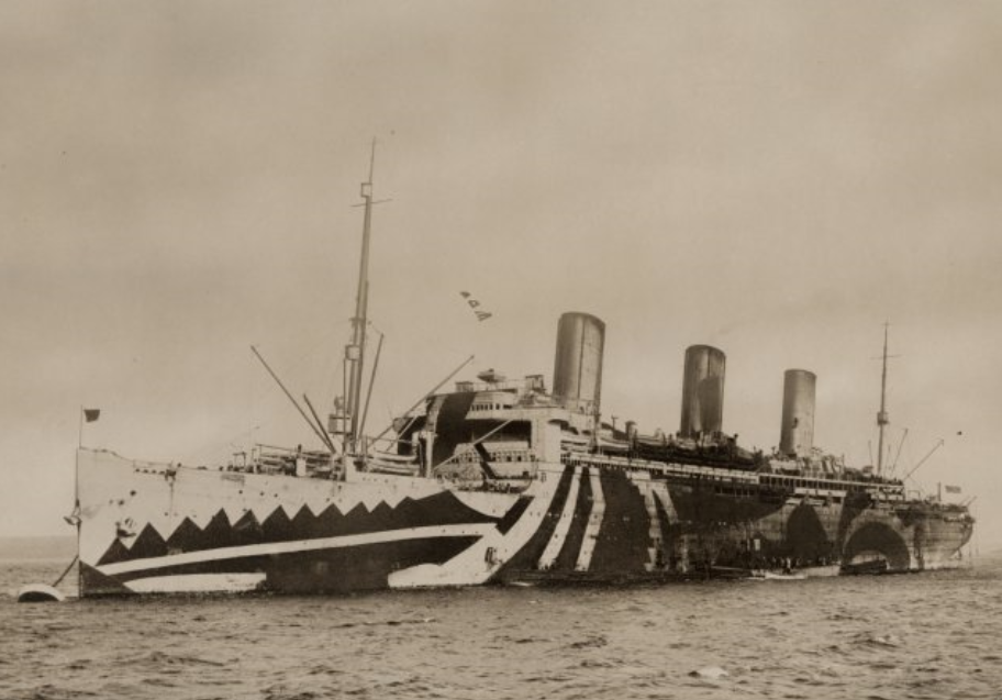Black and white photograph of a battleship from WWI painted with dazzle camouflage, including stripes, swishes, and triangles.