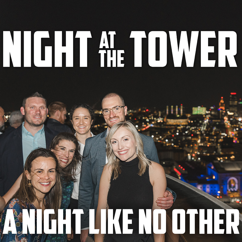 A group of partygoers in cocktail attire pose for a picture at the top of Liberty Memorial Tower with the nighttime Kansas City skyline behind them. Text: 'Night at the Tower / A Night Like No Other'