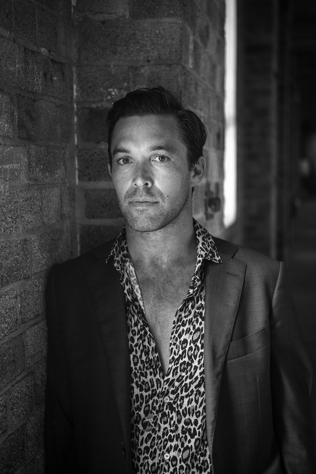 Black and white headshot portrait of a slim, cleanshaven man wearing a button-down shirt and blazer
