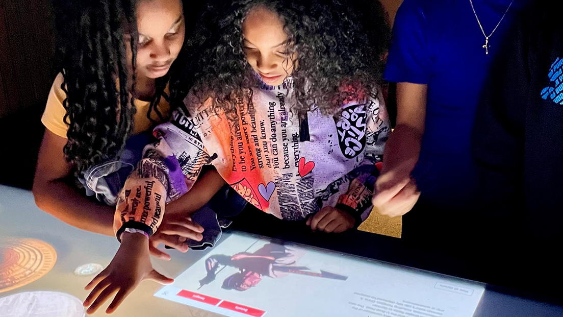 Two Black girls swipe around an interactive table