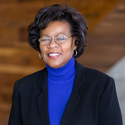 امرأة سوداء في منتصف العمر بشعر قصير كثيف ترتدي كنزة زرقاء برقبة عالية وسترة داكنة