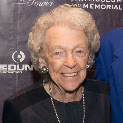 Femme blanche d'un certain âge, aux cheveux blancs bouclés, portant un haut foncé