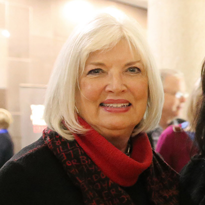 Femme blanche aux cheveux blancs coupés au carré, portant un foulard rouge et une veste sombre