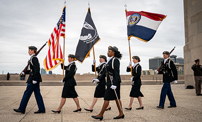 Photo moderne de six jeunes gens en uniforme militaire marchant en rang, portant des drapeaux, des fusils ou des épées.