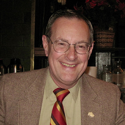Photo of an older white man wearing glasses and a light brown blazer