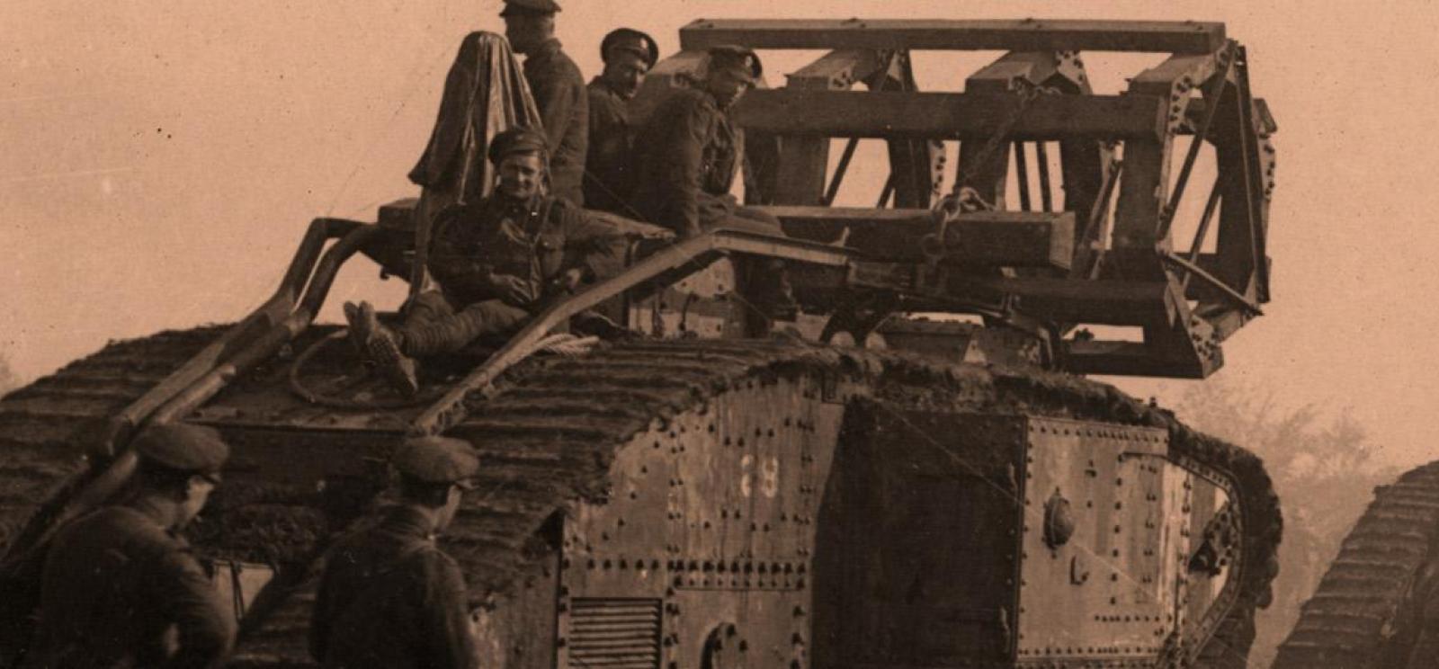 Sepia photograph of a WWI-era tank in a line of tanks. Four men sit on top looking at the viewer.