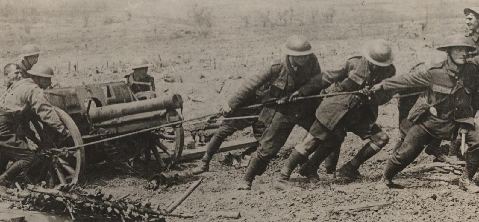 Photographie en noir et blanc d'un groupe d'hommes tirant et poussant un canon de campagne.