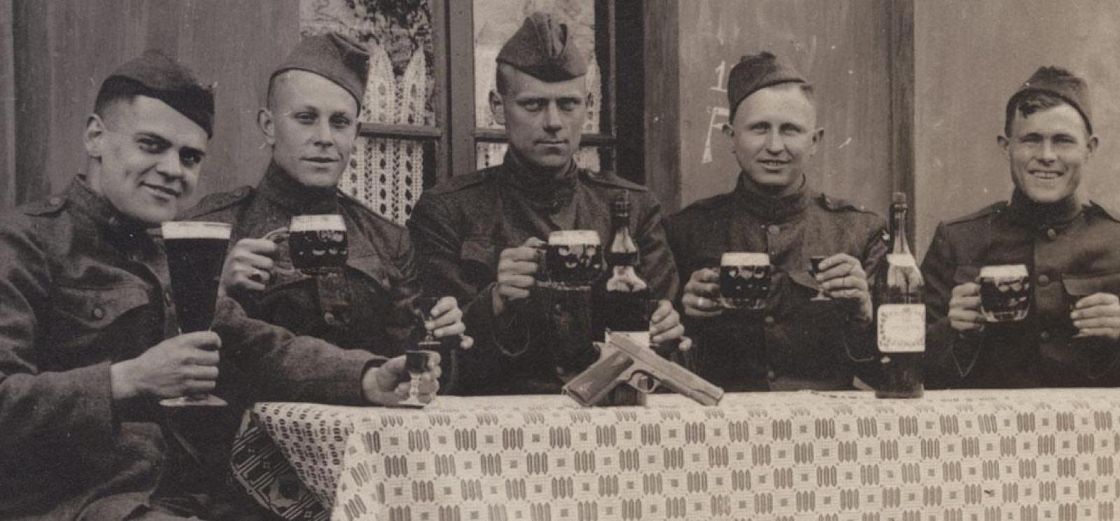 Black and white photograph of WWI-era soldiers sitting in a row facing the camera. They are all raising mugs of beer in a toast.