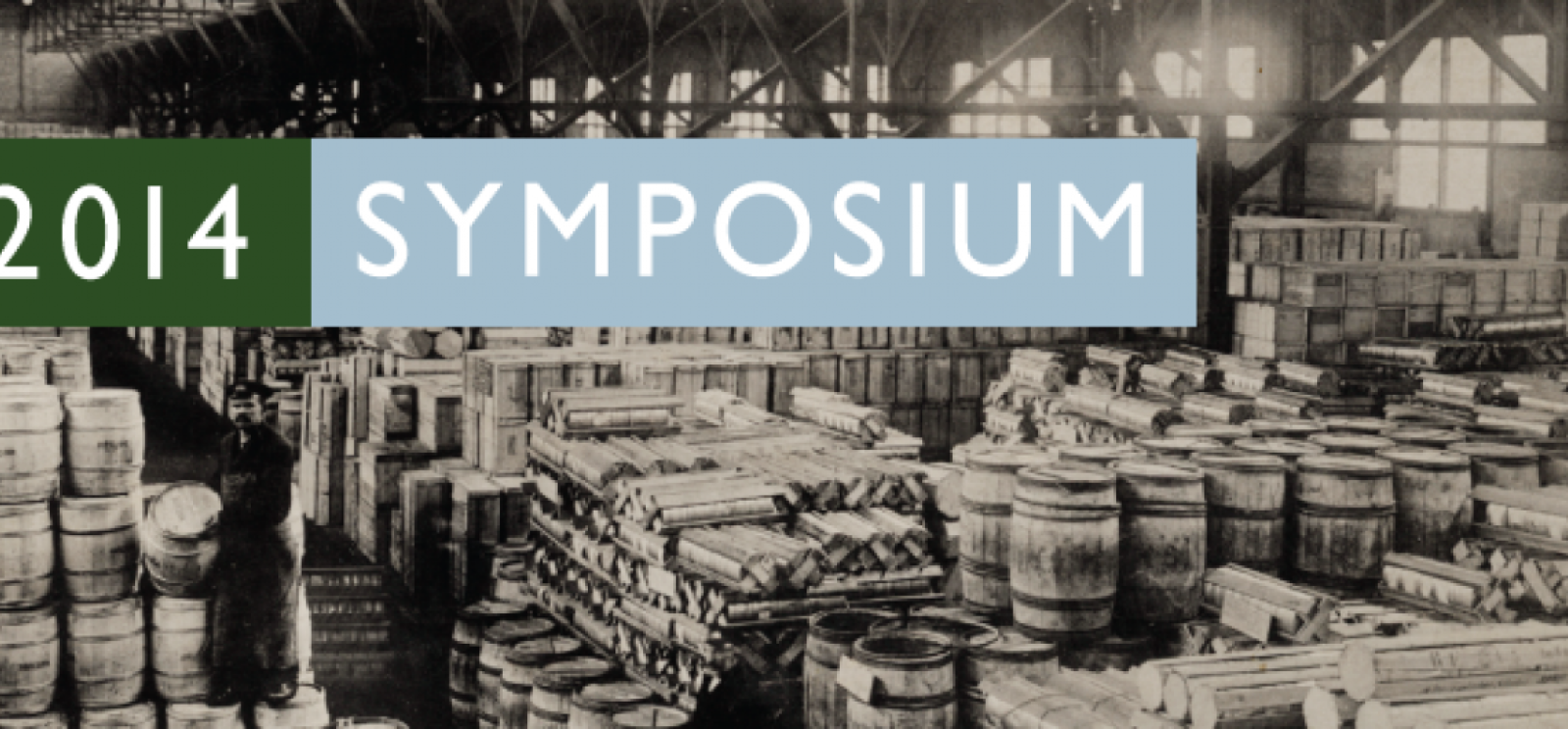 Background image: black and white photograph of pallets and barrels of supplies stacked in rows stretching away from the viewer. Text: 2014 Symposium