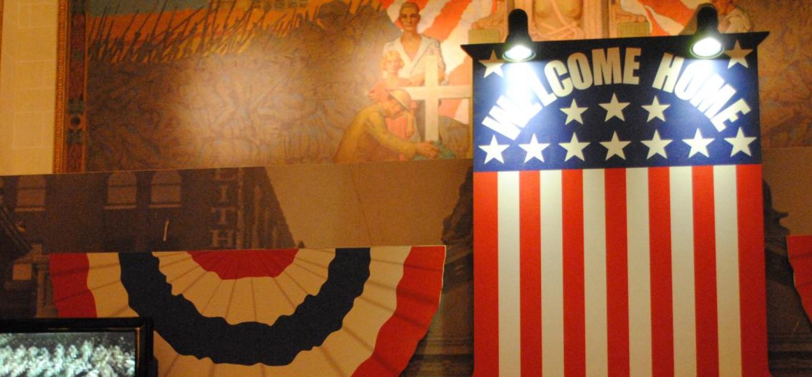 Photograph of a museum display of a signboard done up like the US flag and with the words "Welcome Home."
