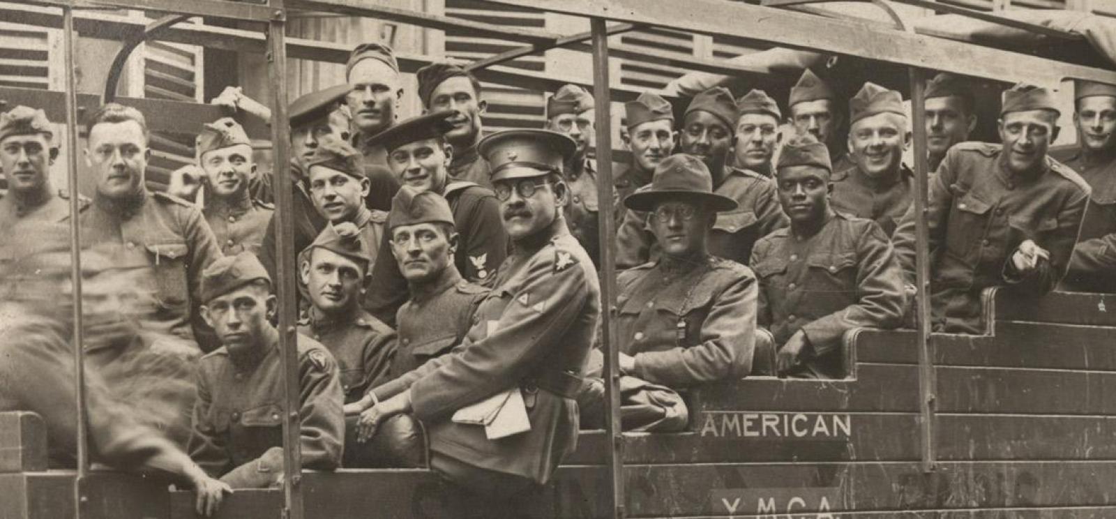 Black and white photo of a large group of men in military uniform seated in a tour bus in a French town.