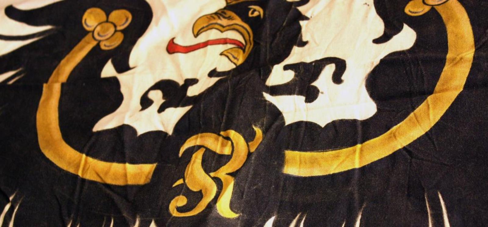 Photograph of an old Prussian flag: a stylized black and gold eagle on a cream field.