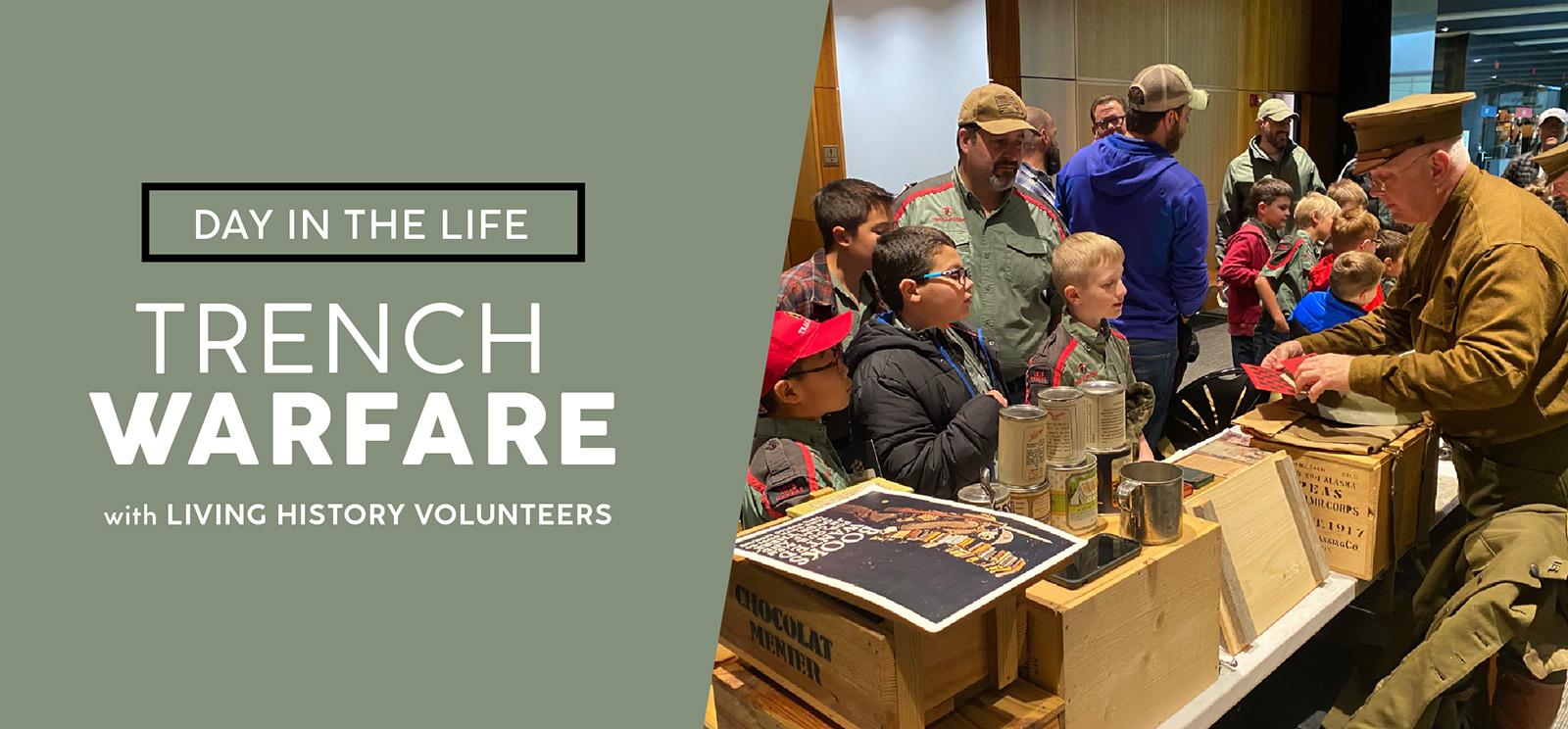 Image: Modern photograph of children gathered in front of a long table filled with WWI-era artifacts and reproductions. A man dressed in WWI-era uniform demonstrates with one of the artifacts in his hands. Text: Day in the Life / Trench Warfare