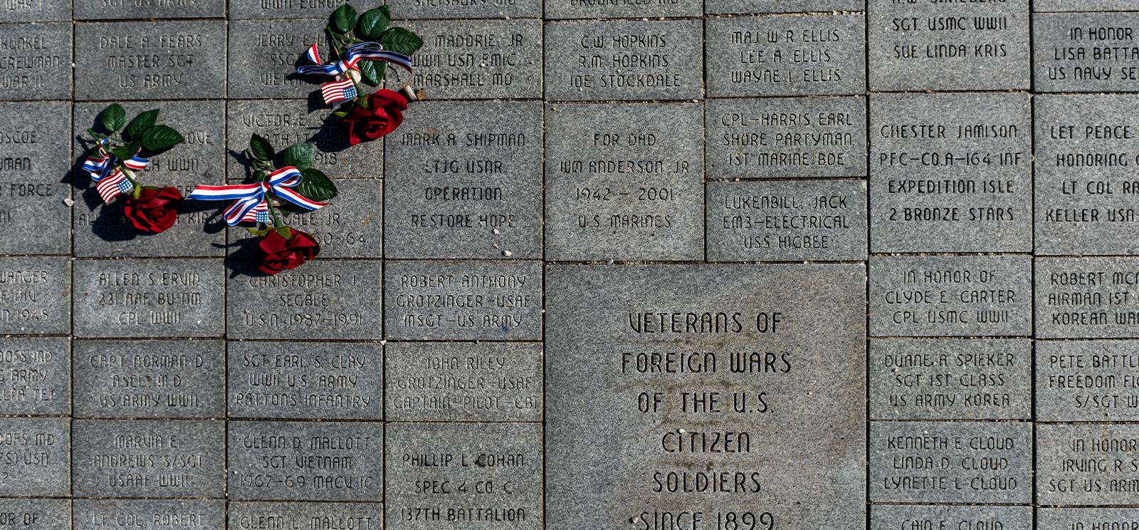 Three red flowers lying on embedded grey bricks. Each brick is inscribed with a dedication.