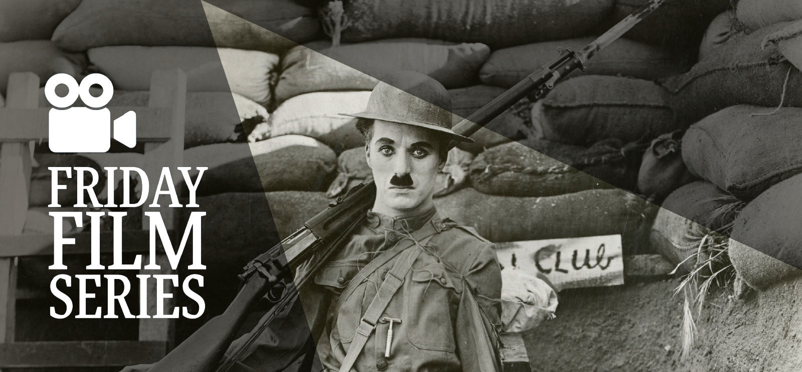 Black and white promotional still of Charlie Chaplin dressed in WWI uniform with a rifle over his shoulder standing in a trench. Text: Friday Film Series