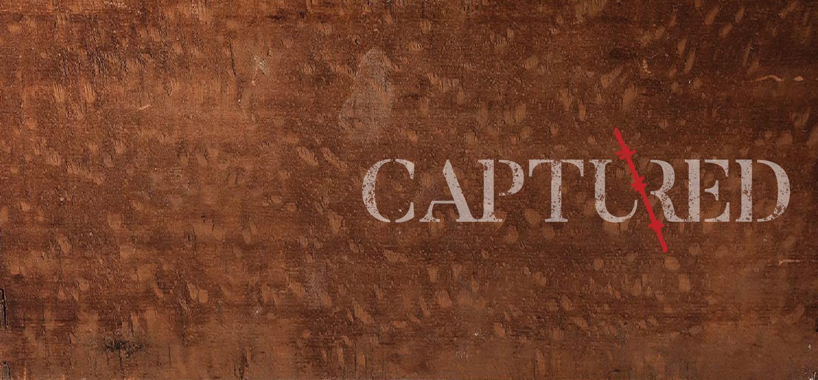Text: 'Captured' in distressed typewriter font on wood background with a red barbed wire slash through the middle