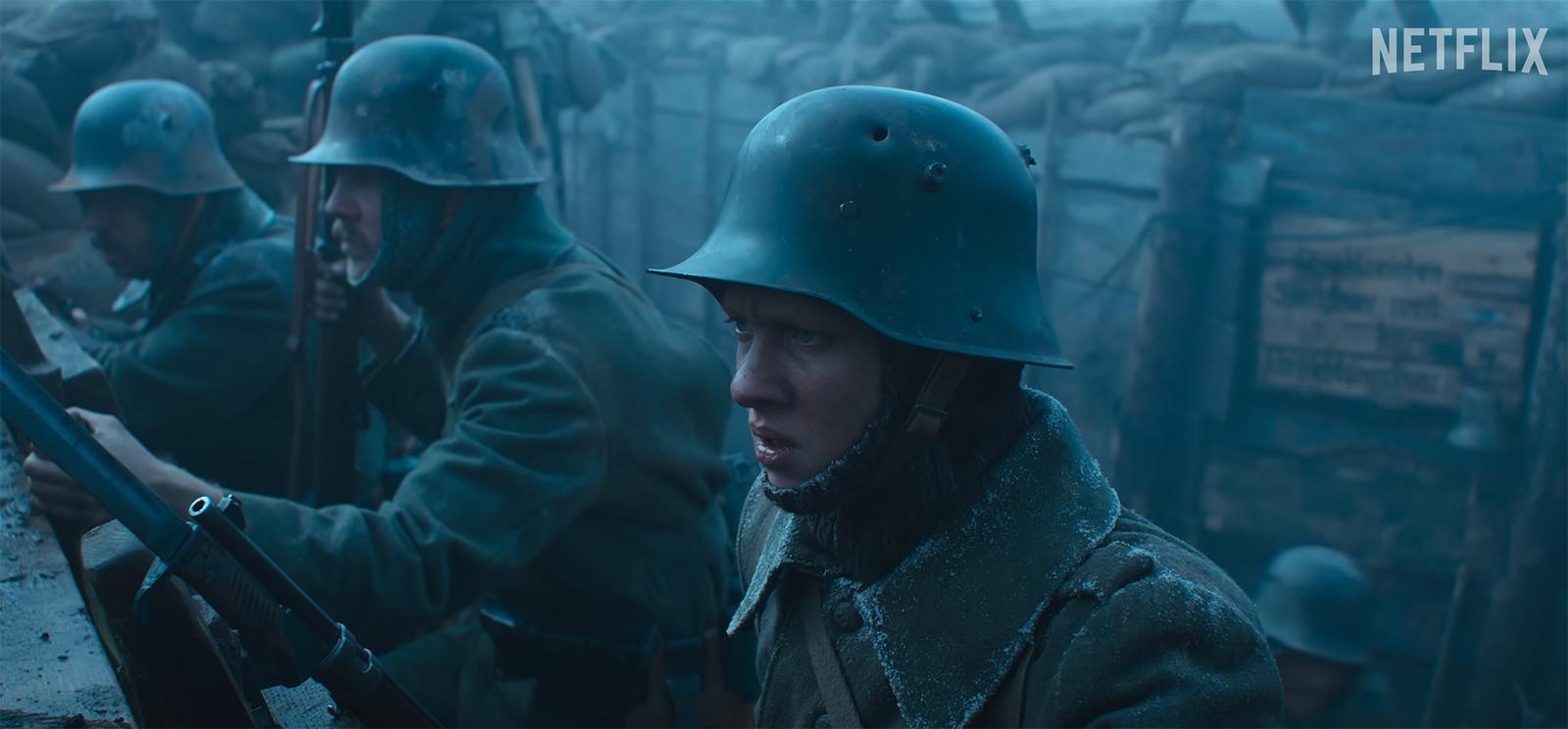 Screenshot from a movie: young white men wearing steel helmets lined up in the rain in a trench.