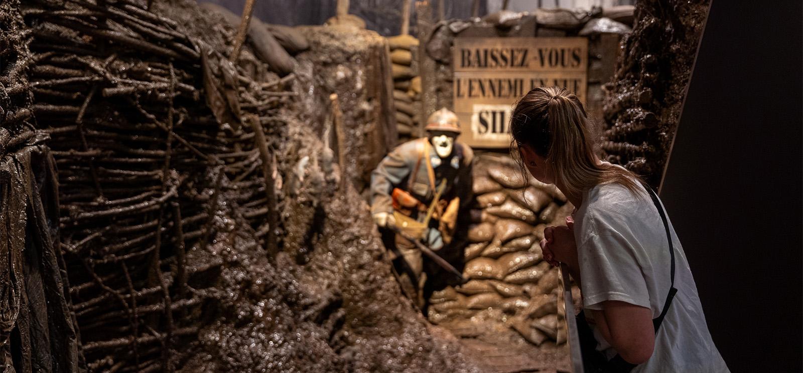 Modern photograph of a girl leaning into a life-size museum exhibit depicting a WWI soldier charging into a trench