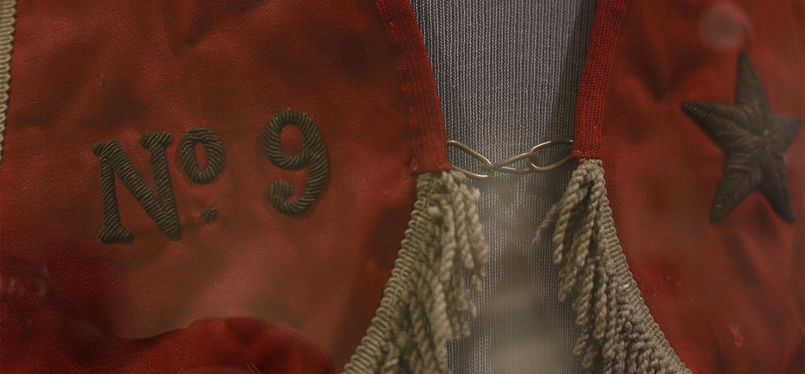 Close-up detail on a red silk stole with gold fringe trim and an embroidered star and "No. 9"