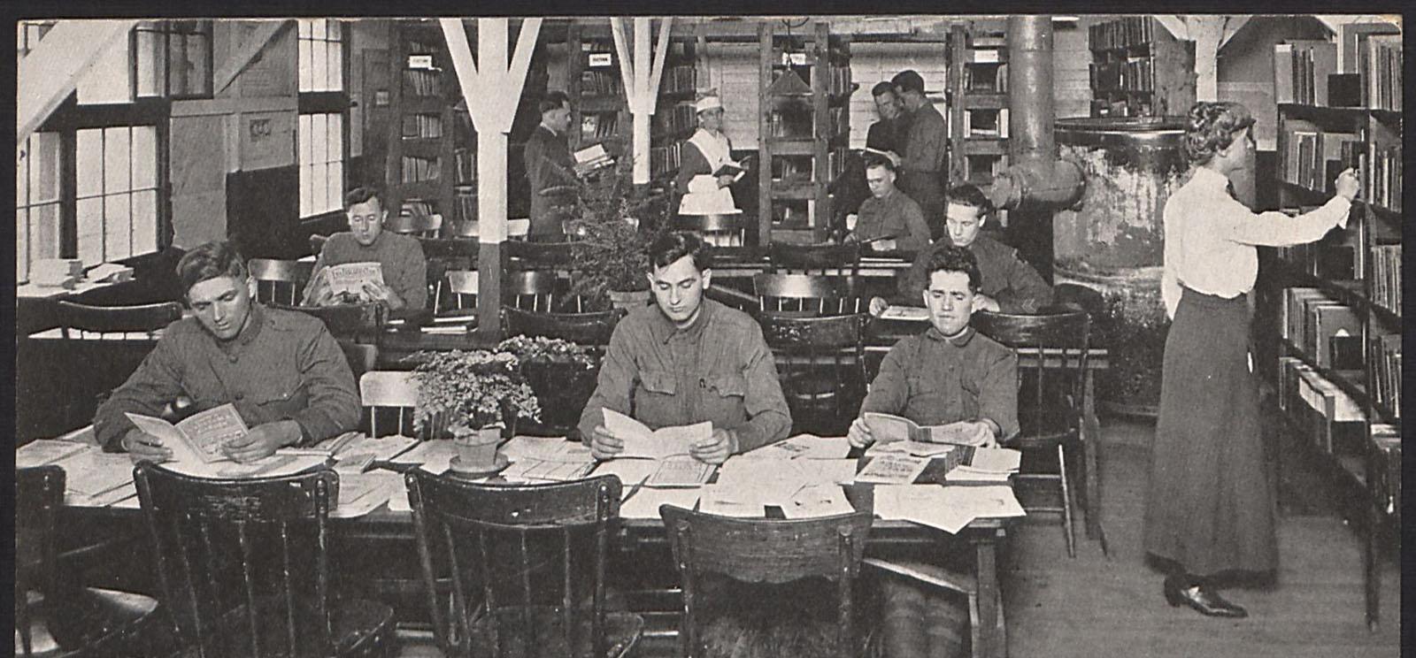 Black and white photo of soldiers in uniform sitting at tables in a library covered in books