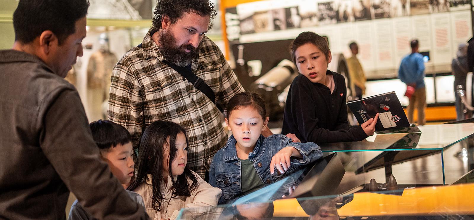 Deux adultes et quatre enfants se rassemblent autour des vitrines d'un musée dans une galerie.