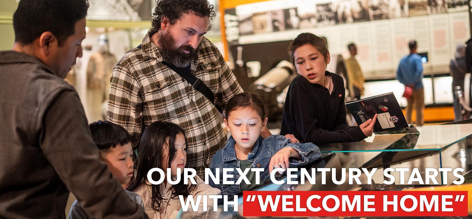 Four children and two adults gather around a touchscreen display and exhibit case in the Main Gallery. Text: "Our next century starts with 'Welcome Home'"