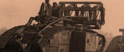 Sepia photograph of a WWI-era tank in a line of tanks. Four men sit on top looking at the viewer.