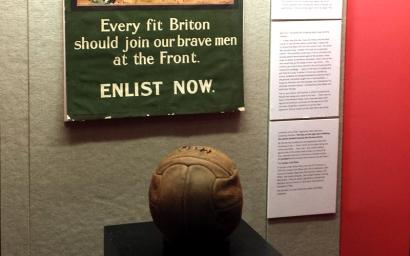 Photo of an old leather soccer ball or football in a museum display case.