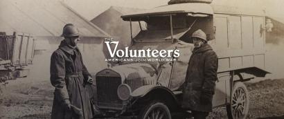 Image: two men dressed in thick overcoats and steel helmets stand next to a WWI-era truck. Text: The Volunteers. Americans Join World War I.