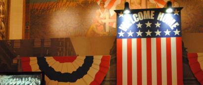 Photograph of a museum display of a signboard done up like the US flag and with the words "Welcome Home."