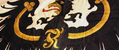Photograph of an old Prussian flag: a stylized black and gold eagle on a cream field.