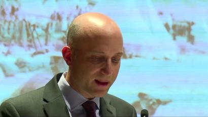 Close-up on a bald light-skinned man giving a presentation with the screen behind him.