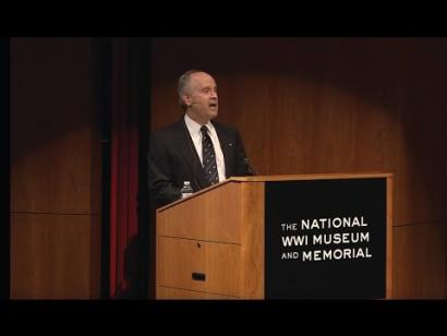 Video still of an older white man presenting at the podium on the Museum auditorium stage.