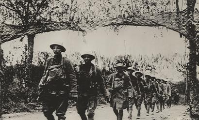 Black and white photograph of a line of Black American WWI soldiers walking through the woods