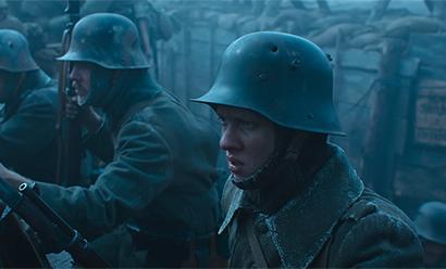 Screenshot from a movie: young white men wearing steel helmets lined up in the rain in a trench.