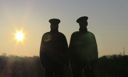 Two people in WWI uniform stand silhouetted against a sunrise