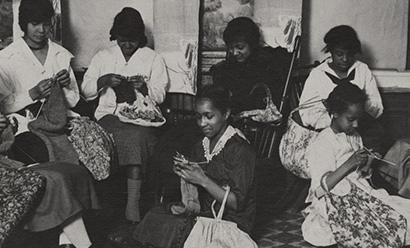 Photographie en noir et blanc d'un groupe de femmes noires réunies dans une pièce en train de tricoter divers projets