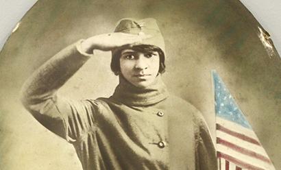 Sepia photograph of a Black woman in cap and uniform saluting while holding a U.S. flag.