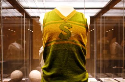 Modern photograph of a yellow and green basketball uniform displayed in a glass case.