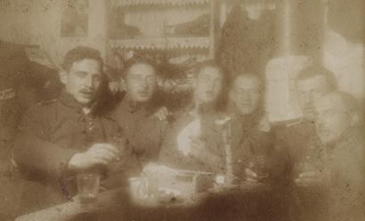 Fuzzy sepia picture of a group of soldiers seated around a table scattered with drinks and toasting the camera