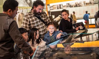 Two adults and four children gather around glass museum cases in a gallery
