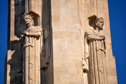 Photograph of two sculpted figures attached to a stone structure with wings, helmets, and holding swords.