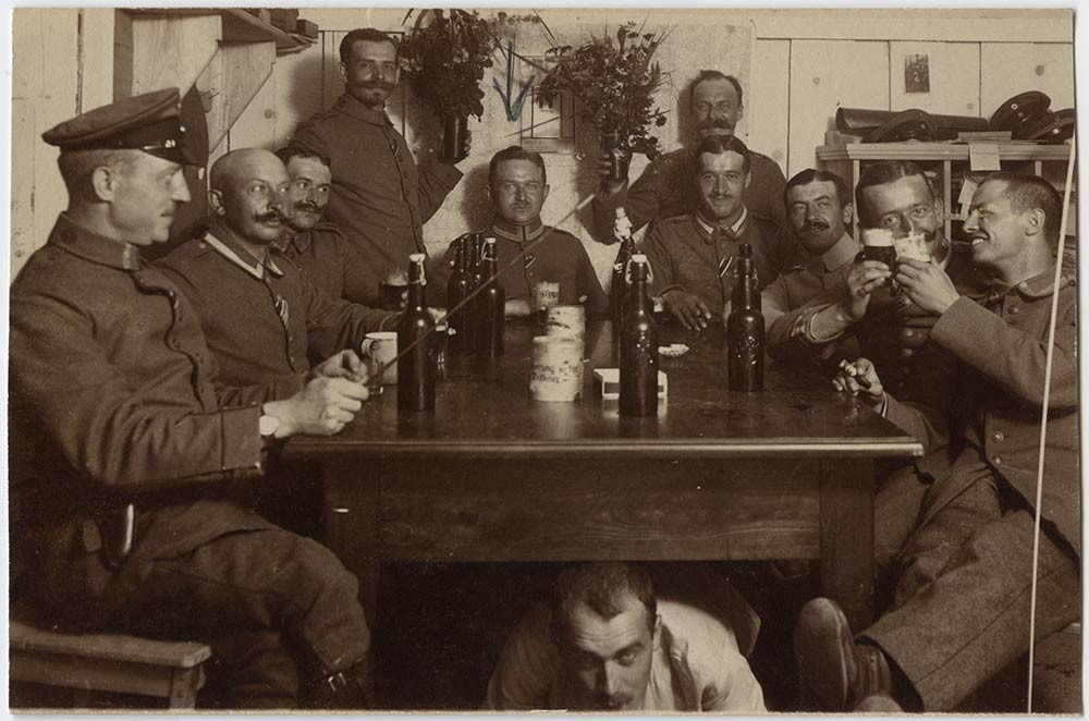 Photo en noir et blanc d'un groupe bruyant de soldats allemands rassemblés autour et sous une table buvant des bouteilles de bière. 