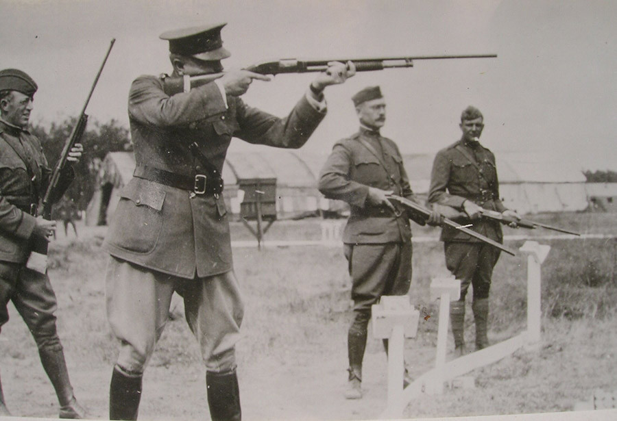 Photographie en noir et blanc de quatre hommes en uniforme militaire tenant des fusils. Celui au premier plan a son fusil tiré sur une cible invisible. Les trois autres observent.