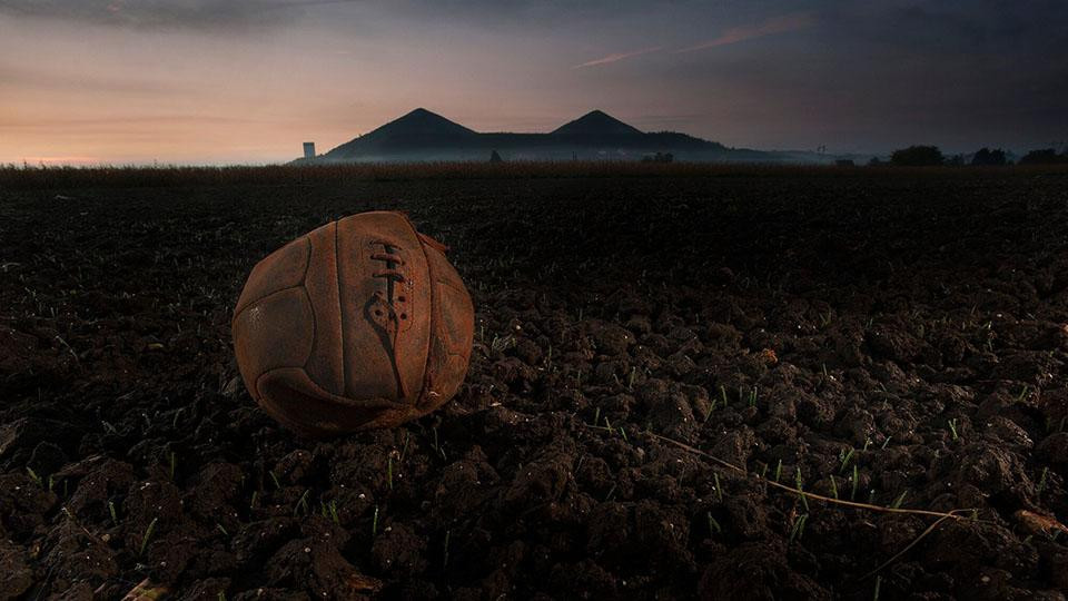 Photographie d'un vieux ballon de soccer ou de football en cuir dans un champ vide au coucher du soleil.