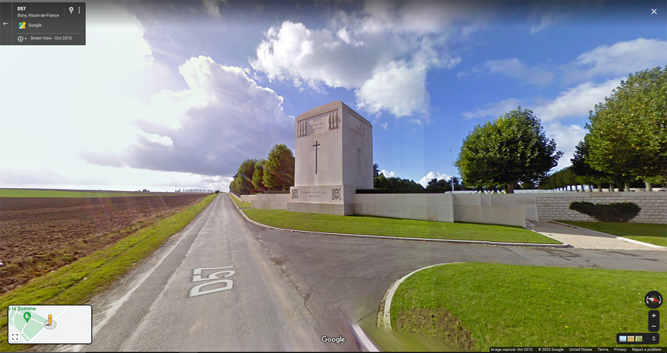 Google Street View لطريق يمر عبر نصب حجري مربع كبير عند مدخل المقبرة.