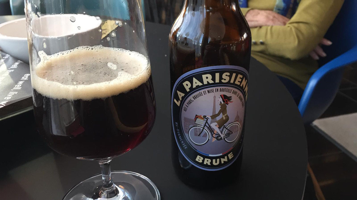 زجاجة بيرة "La Parisienne Brune" بجوار كأس بيرة منبع