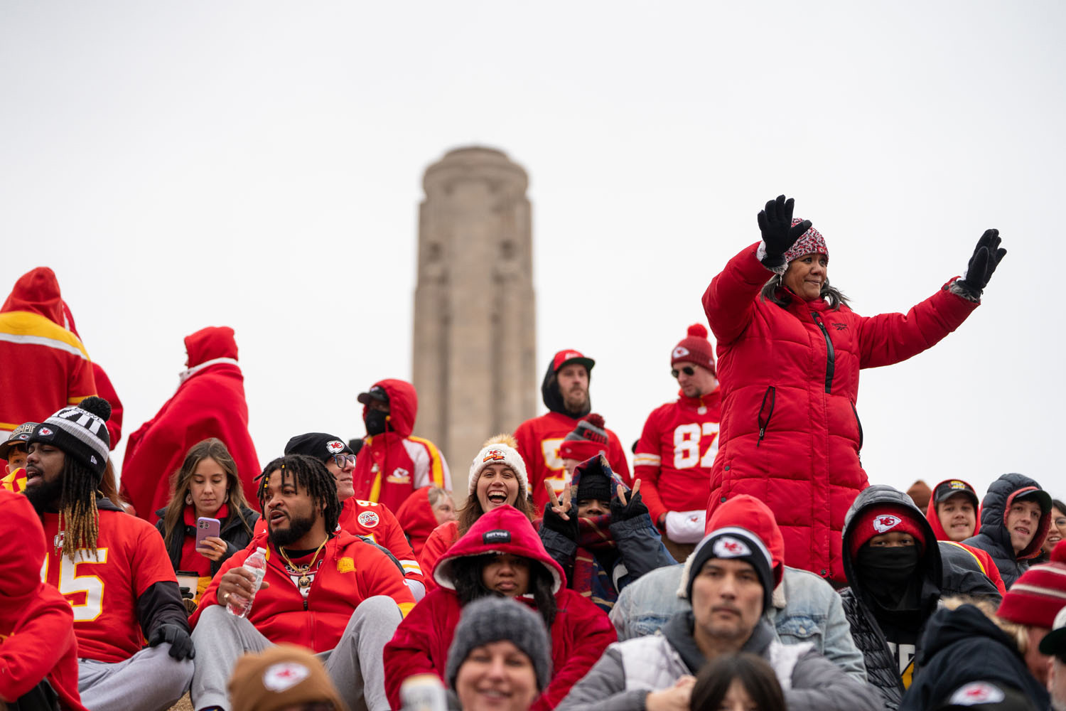 Photographie moderne d'une foule de personnes vêtues de vêtements d'hiver rouges. Une personne vêtue d'un manteau bouffant rouge se tient debout, les bras levés. La Liberty Memorial Tower est en arrière-plan.