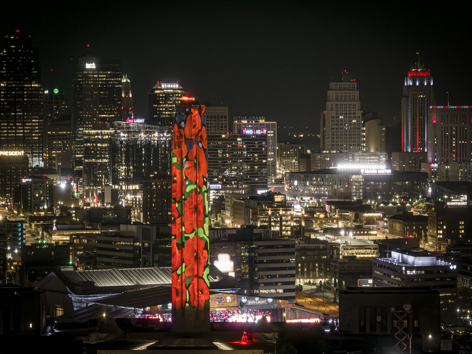Photographie moderne prise la nuit. La Liberty Memorial Tower est au premier plan, éclairée par des projections de coquelicots. La ligne d'horizon du centre-ville de Kansas City est en arrière-plan, illuminée avec brio.
