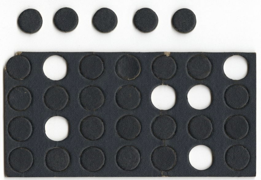 Photographie moderne d'un morceau rectangulaire de carton épais enduit de peinture noire, perforé de nombreux cercles. Certains cercles ont été arrachés et placés sur le côté. 